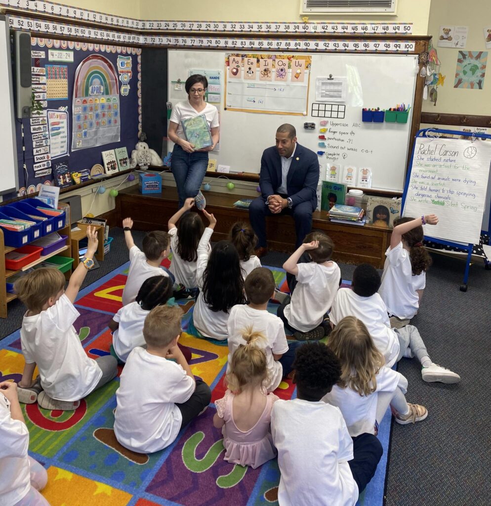 Sean spiller sitting in an elementary school classroom speaking with a group of 15 elementary school students